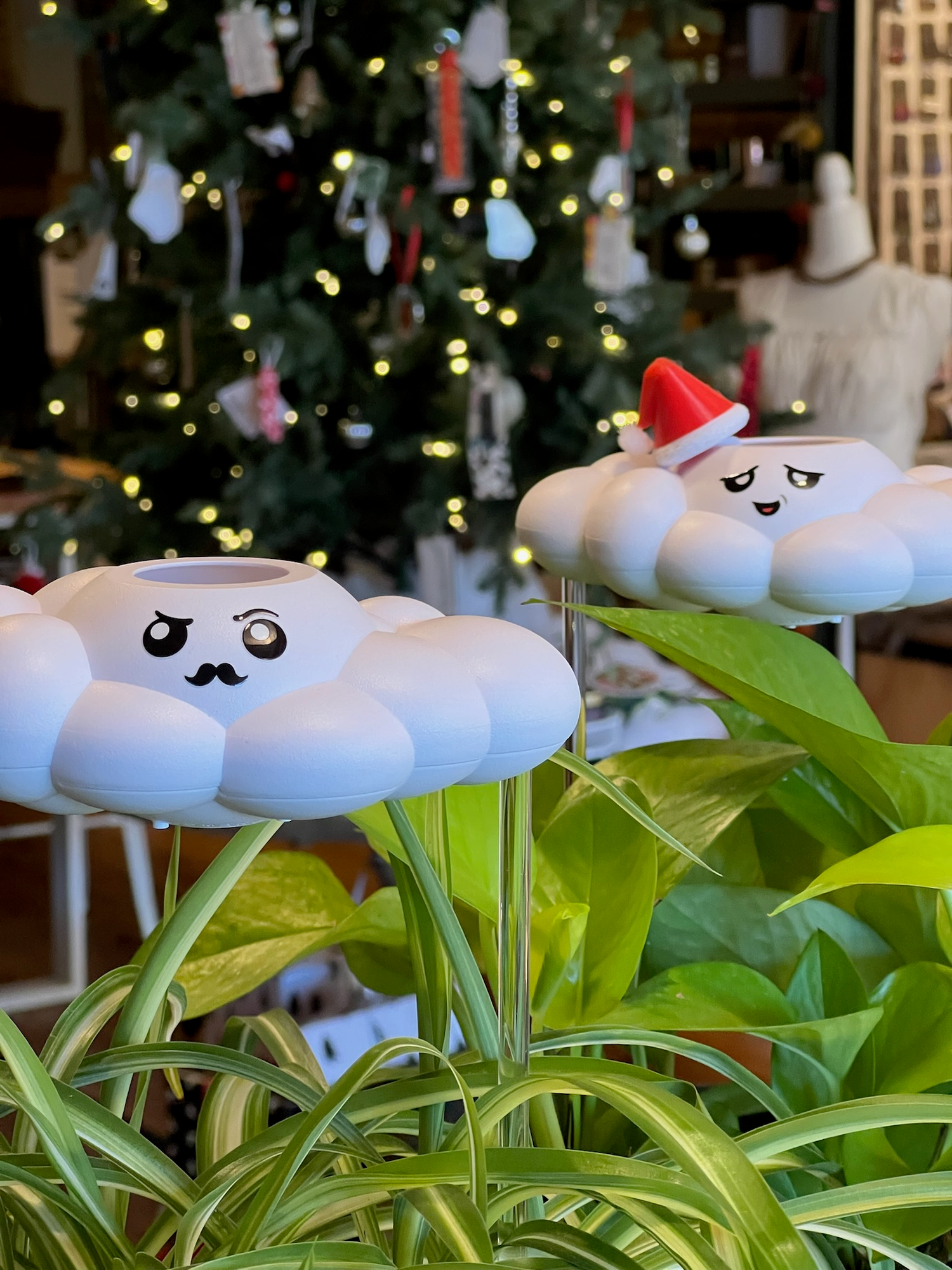 Two original dripping rain clouds inside plants in front of a christmas tree.